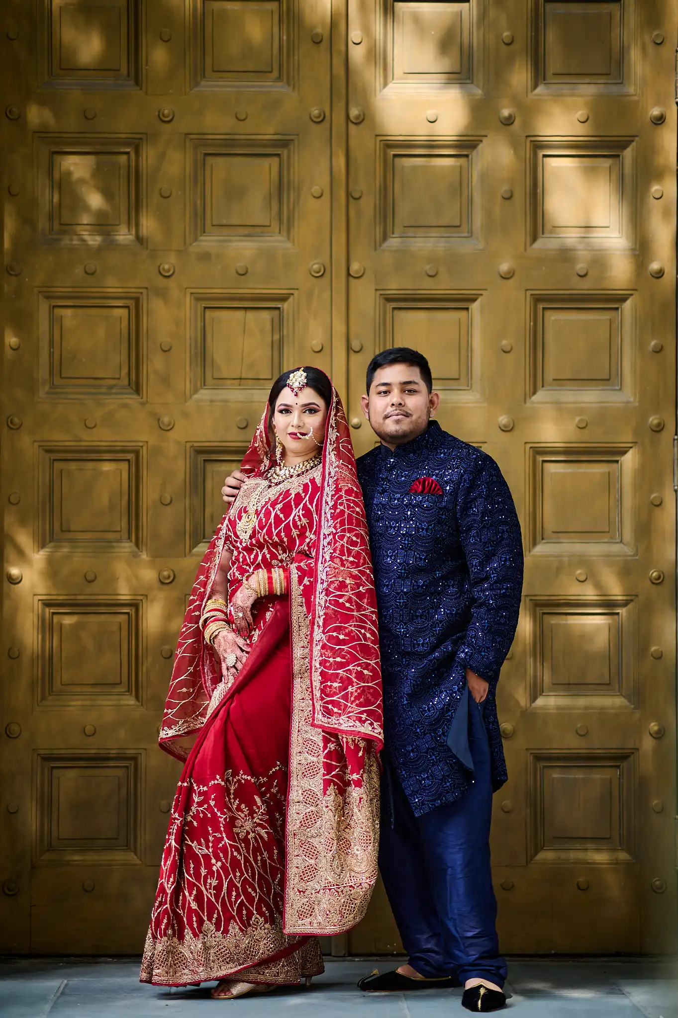 Bride and groom in yellow Haldi attire sharing a Maaza juice box in front of a marigold flower curtain